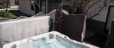 Un bain à remous dans un jardin, avec une terrasse en bois, entouré d’arbres et d’une maison.