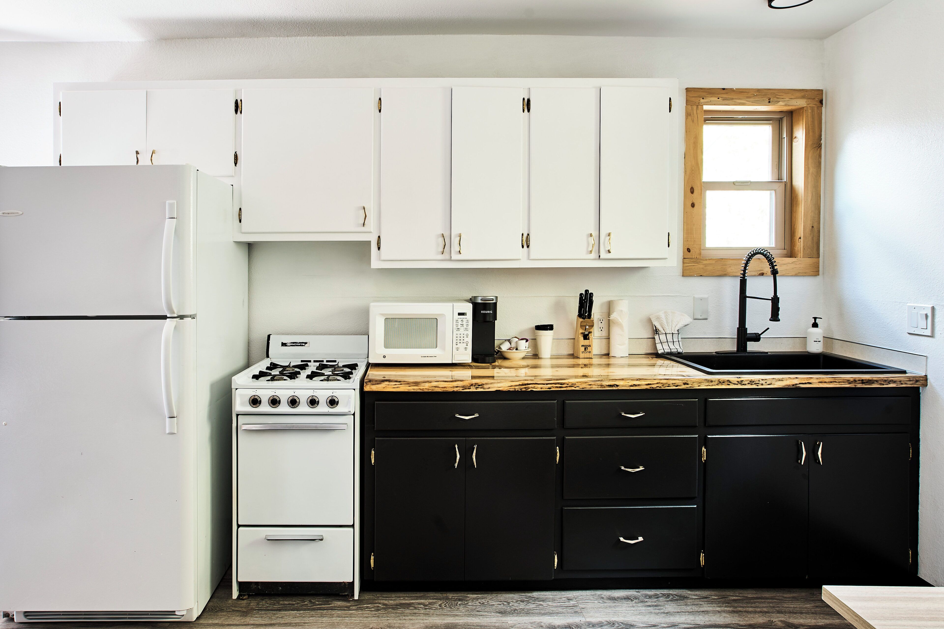 A kitchen with white cabinets, a stove, a microwave, a sink, and a window above the sink.