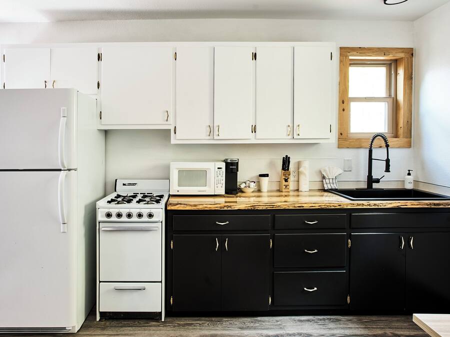 A kitchen with white cabinets, a stove, a microwave, a sink, and a window above the sink.