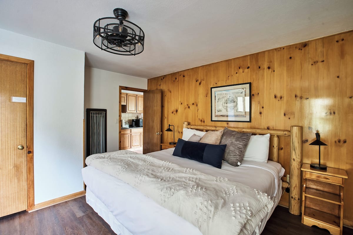 Una camera da letto con testiera in legno, un letto con biancheria bianca, un comodino con una lampada e un quadro appeso al muro.