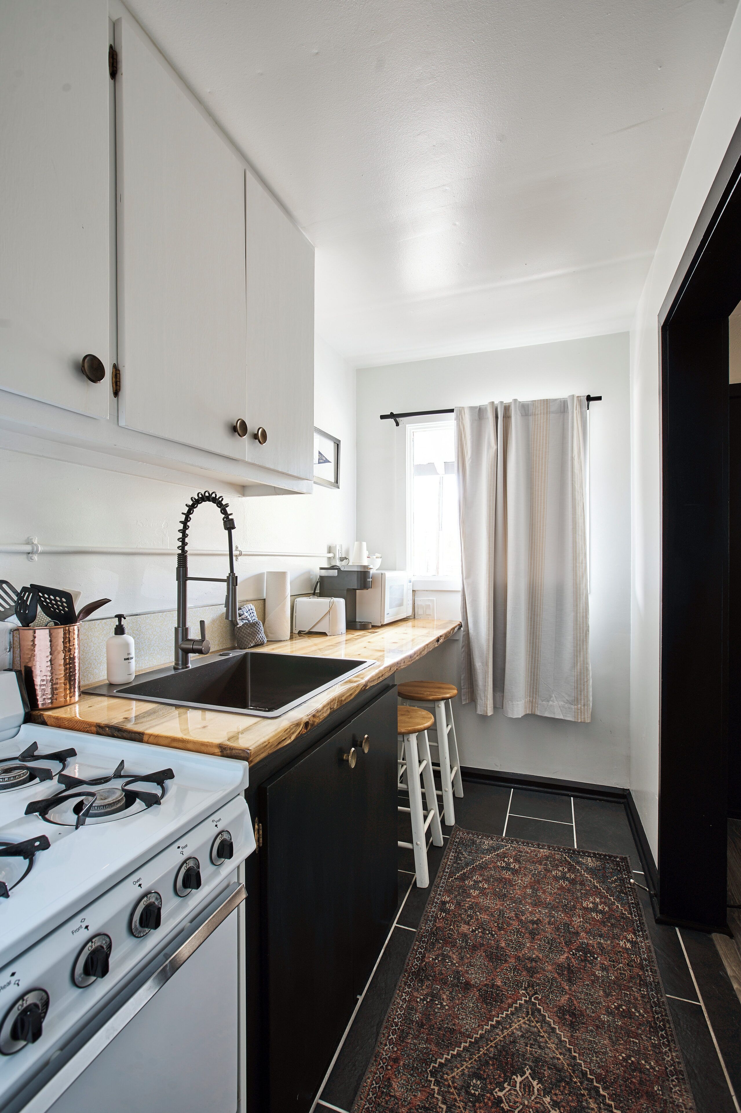 Una cocina compacta con estufa a gas, un lavabo y una ventana con cortinas.