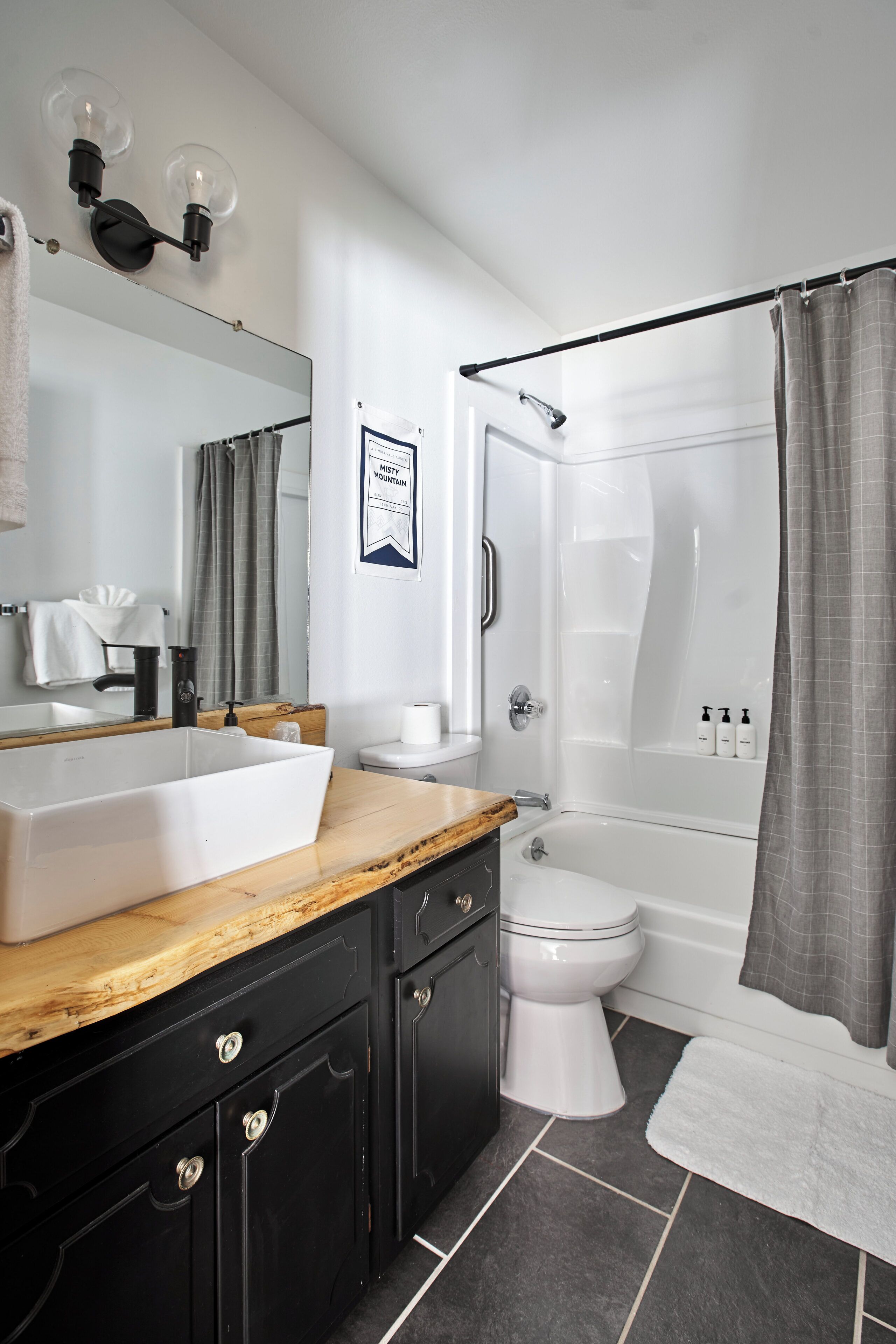 A modern bathroom with a large sink, dark cabinetry, a mirror, a toilet, a shower, and a towel rack.