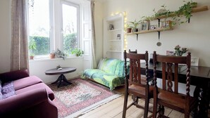 Un salon chaleureux avec un canapé, un canapé vert, une chaise en bois, une petite table et une bibliothèque agrémentée de plantes et de photos.