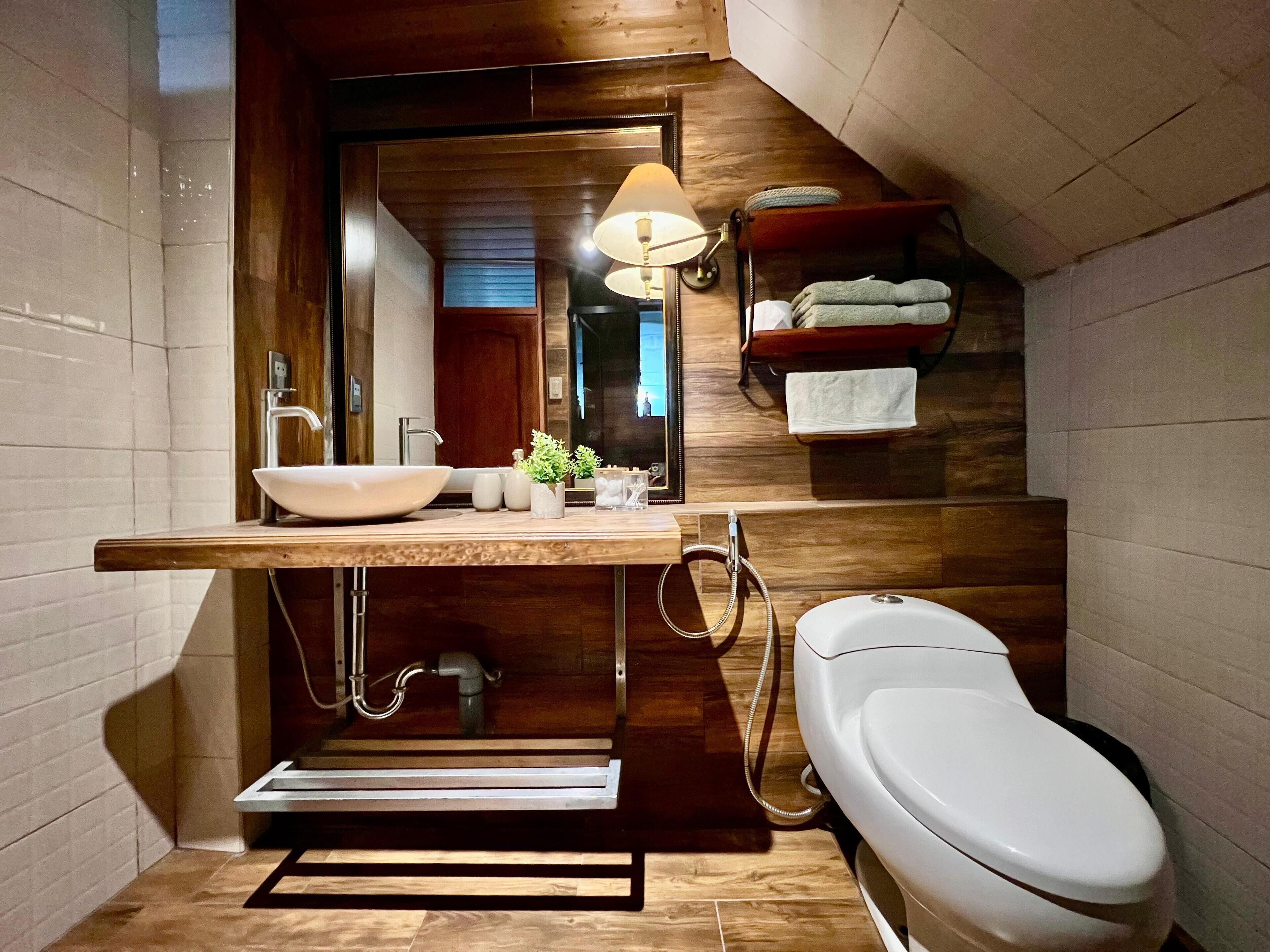 Un baño moderno con tocador de madera, lavabo sobre encimera, inodoro y toallero.
