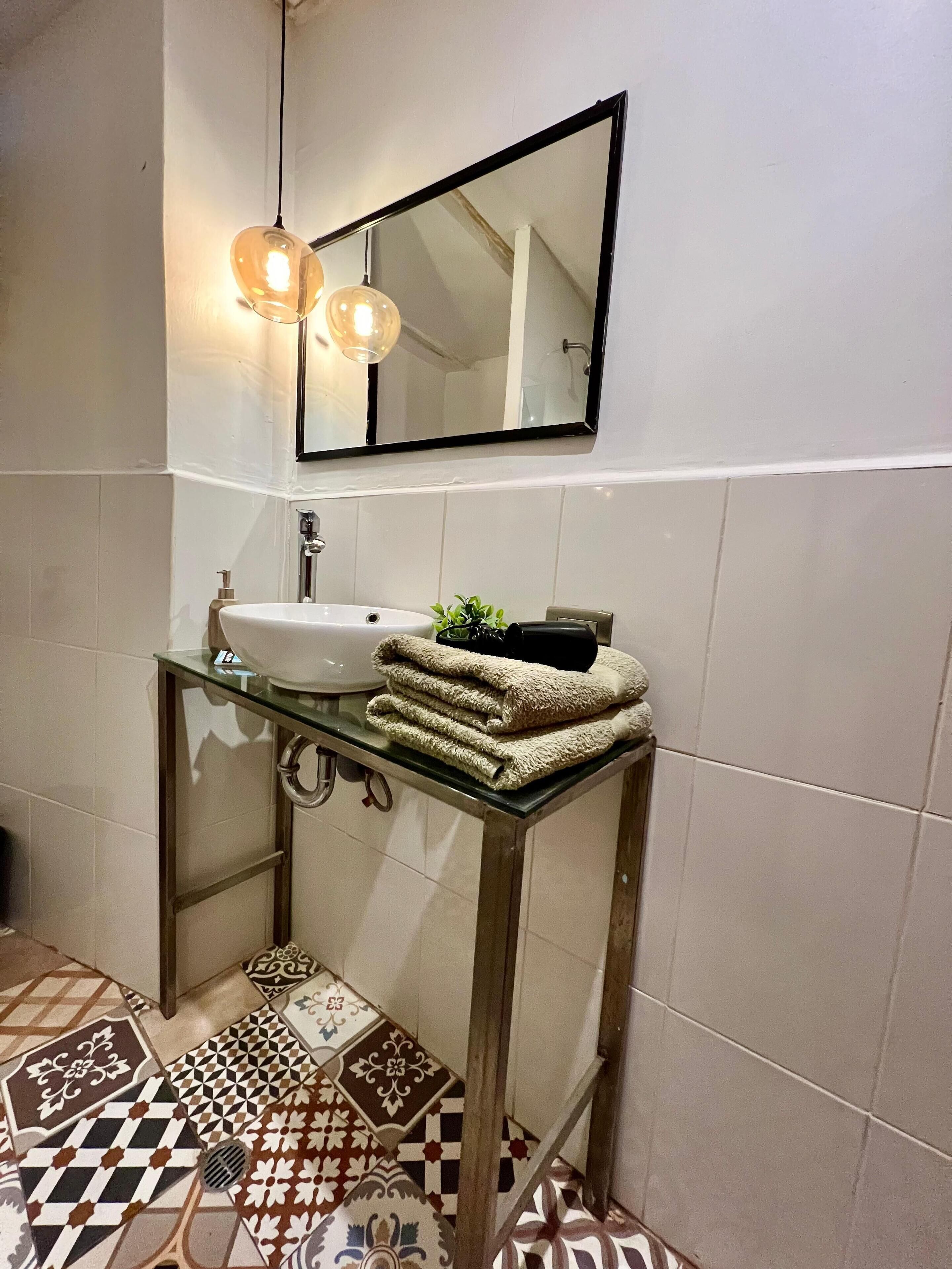 A bathroom with a glass sink, a mirror, and a patterned floor.