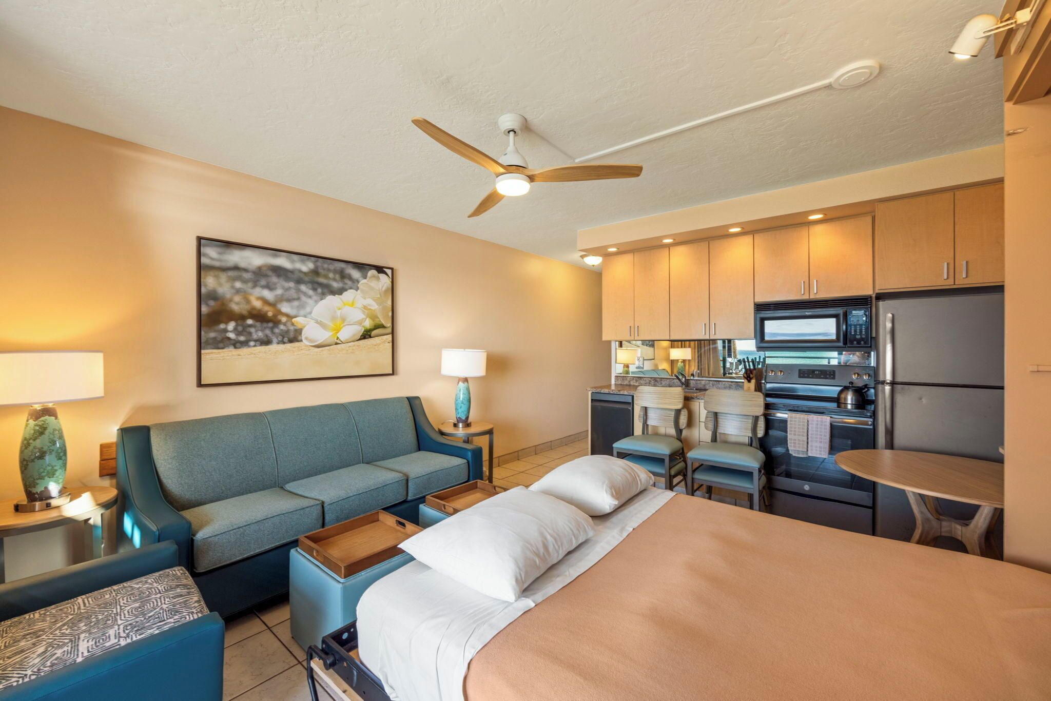 A hotel room with a bed, a sofa, a desk, a microwave, a refrigerator, and a ceiling fan.