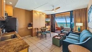 A modern hotel room with a kitchen, dining area, and a balcony with a view of the ocean.