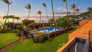 A pool area with lounge chairs, palm trees, and a view of the ocean at sunset.