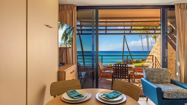 A room with a dining table set for two, a blue sofa, and a view of the ocean.