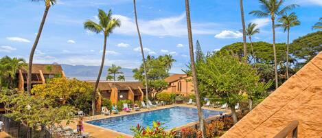 A pool area with lounge chairs, palm trees, and a view of the ocean.