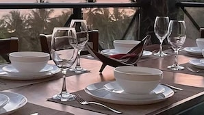 Un tavolo da pranzo apparecchiato per un pasto, con piatti, ciotole e bicchieri da vino, con vista su un tramonto.