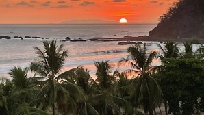 Tramonto su una costa con palme e formazioni rocciose.