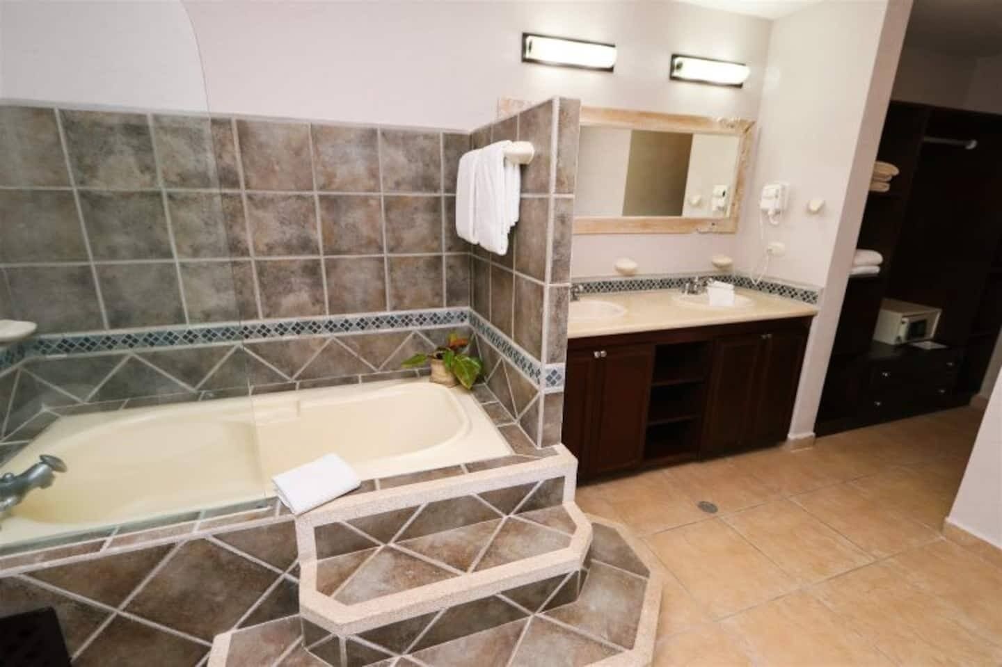 Ein Badezimmer mit einer Badewanne, zwei Waschbecken, einem Spiegel und einem gefliesten Boden.