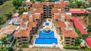 Un resort con piscina centrale, numerosi balconi e un paesaggio circostante con palme.