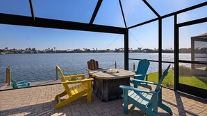 A covered outdoor seating area with Adirondack chairs and a fire pit, overlooking a body of water. - Paradise on the Lake (Cape Coral)