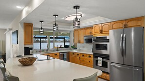 A modern kitchen with wooden cabinets, stainless steel appliances, and a large island with a woven bowl. - Paradise on the Lake (Cape Coral)
