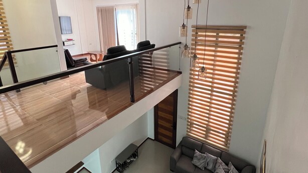 A modern living room with a wooden floor, a sofa, a coffee table, and a dining area with chairs. - Luxury Solar Home where Style Meets Sustainability (Lipa)