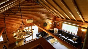 L’intérieur d’un chalet confortable, avec un plafond en bois, un grand lustre, un canapé et une table à manger.