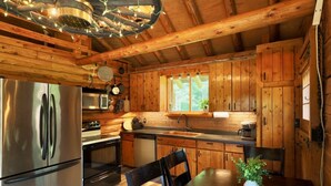 Une cuisine rustique aménagée dans une cabane en bois, comprenant un réfrigérateur, une cuisinière, un évier et une table à manger.