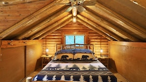 Une chambre à coucher située dans une cabane en rondins, avec un lit, un ventilateur de plafond, une fenêtre et une table de chevet.