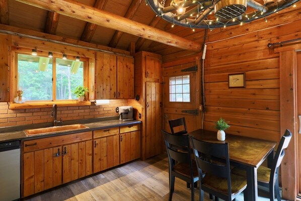 A wooden cabin interior with a kitchen area, dining table, and chairs.