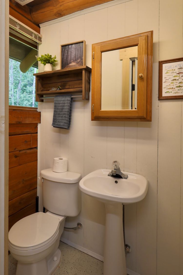 Ein kleines Badezimmer mit Toilette, Waschbecken und Holzregalen über dem Waschbecken.