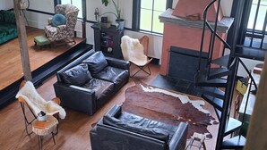 Ein geräumiges Wohnzimmer mit Holzboden, einer schwarzen Ledersofa, einem grünen Sofa, einer Holzbank und einer Treppe.