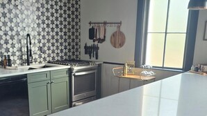 Eine moderne Küche mit einer zentralen Kochinsel, grünen Schränken, einer gemusterten Spritzschutzwand und hängenden Küchenutensilien.