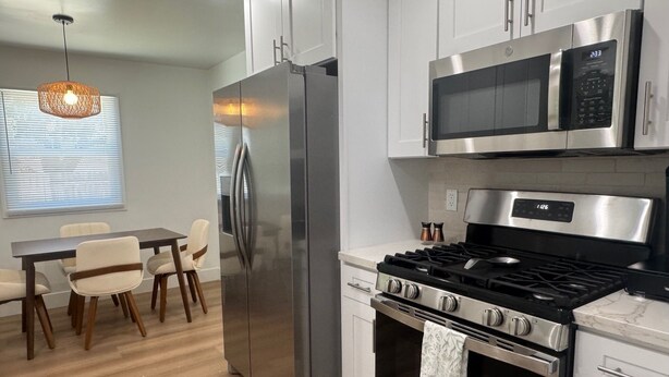 A modern kitchen with stainless steel appliances, a dining area with wooden chairs, and a pendant light. - Beach cottage-5 blocks from the sand. (Port Hueneme)