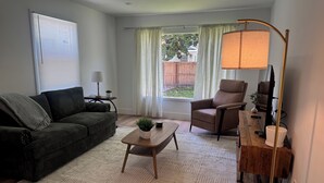 A living room with a sofa, armchair, coffee table, lamp, and a view of the outdoors through a window. - Beach cottage-5 blocks from the sand. (Port Hueneme)