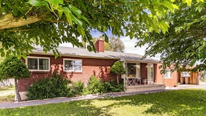A red brick house with a front porch, a small lawn, and a tree providing shade.