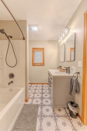 Un baño con bañera, ducha, lavamanos, espejo y ventana.