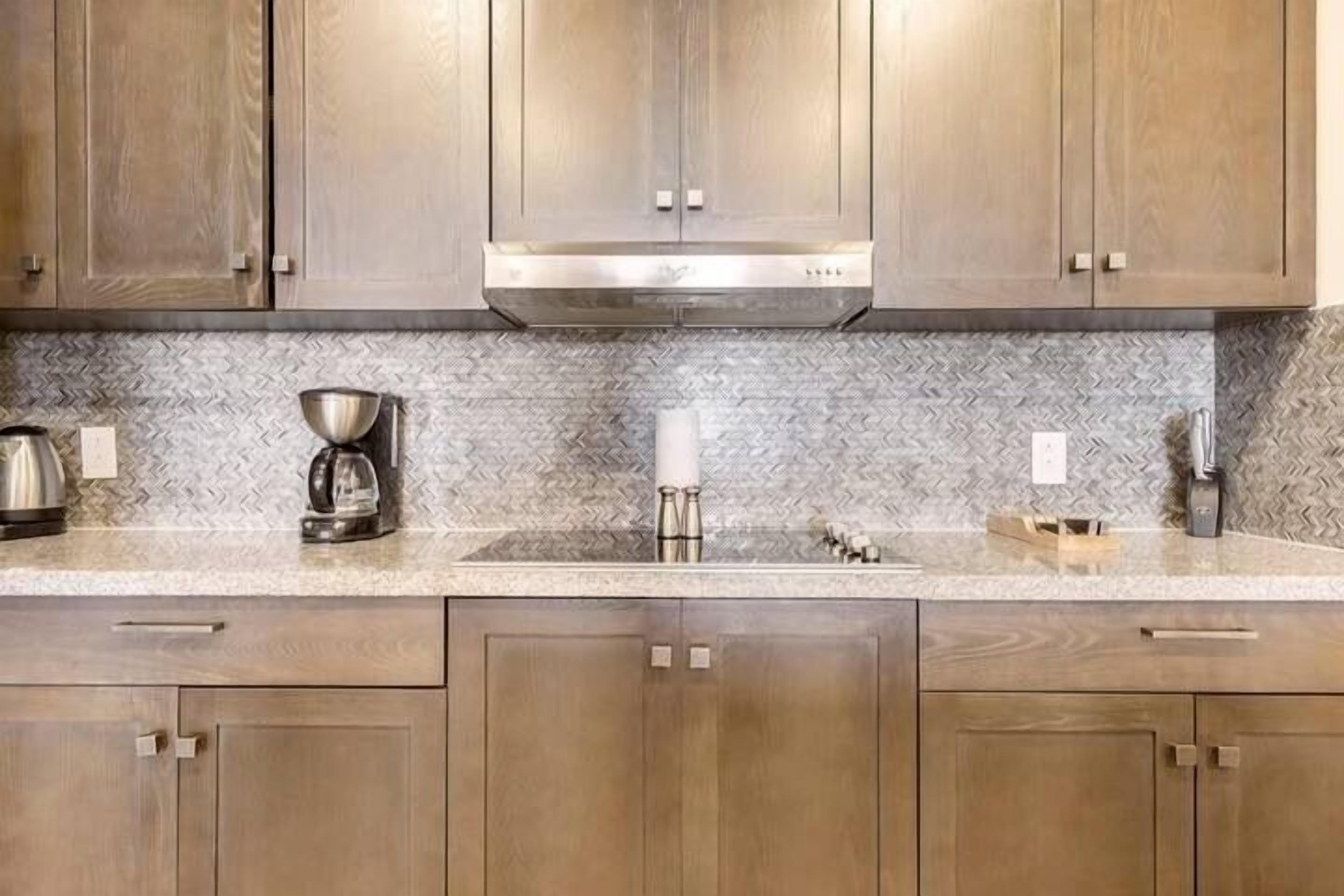 A kitchen with wooden cabinets, a herringbone backsplash, and stainless steel appliances.