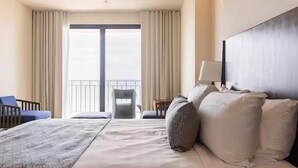 A hotel room with a large bed, a chair, a desk, and a view of the outdoors.