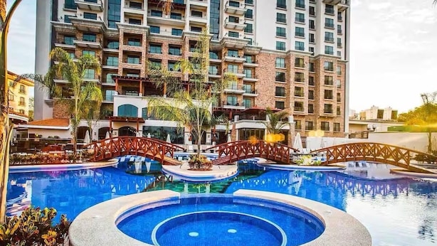 A swimming pool with a bridge, surrounded by a multi-story building with balconies.
