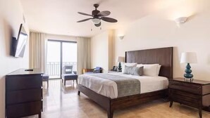 A hotel room with a large bed, a desk, a chair, a ceiling fan, and a view of the outdoors.