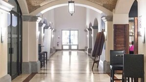 A spacious hallway with a high, arched brick ceiling and a central light fixture. There are seating areas on either side and a large window at the end of the hallway.