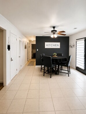 A kitchen with a ceiling fan, a dining table with chairs, and a black wall with a 'KITCHEN' sign.