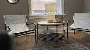 A room with two upholstered chairs, a small round table, a lamp, and a framed picture on the table.