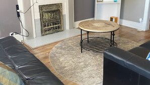 A living room with a fireplace, a round table, a sofa, and a television mounted on the wall.