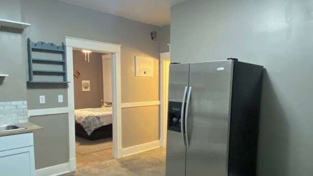 A compact kitchen with a stainless steel refrigerator, a small countertop, and a door leading to a bedroom.