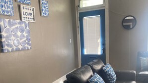 A living room with a black leather sofa, a blue-framed window, and wall art including a 'LOVE' sign.