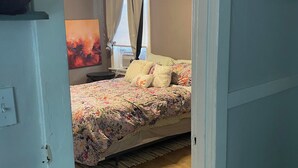 A bedroom with a bed, a ceiling fan, a window with curtains, and a painting on the wall.