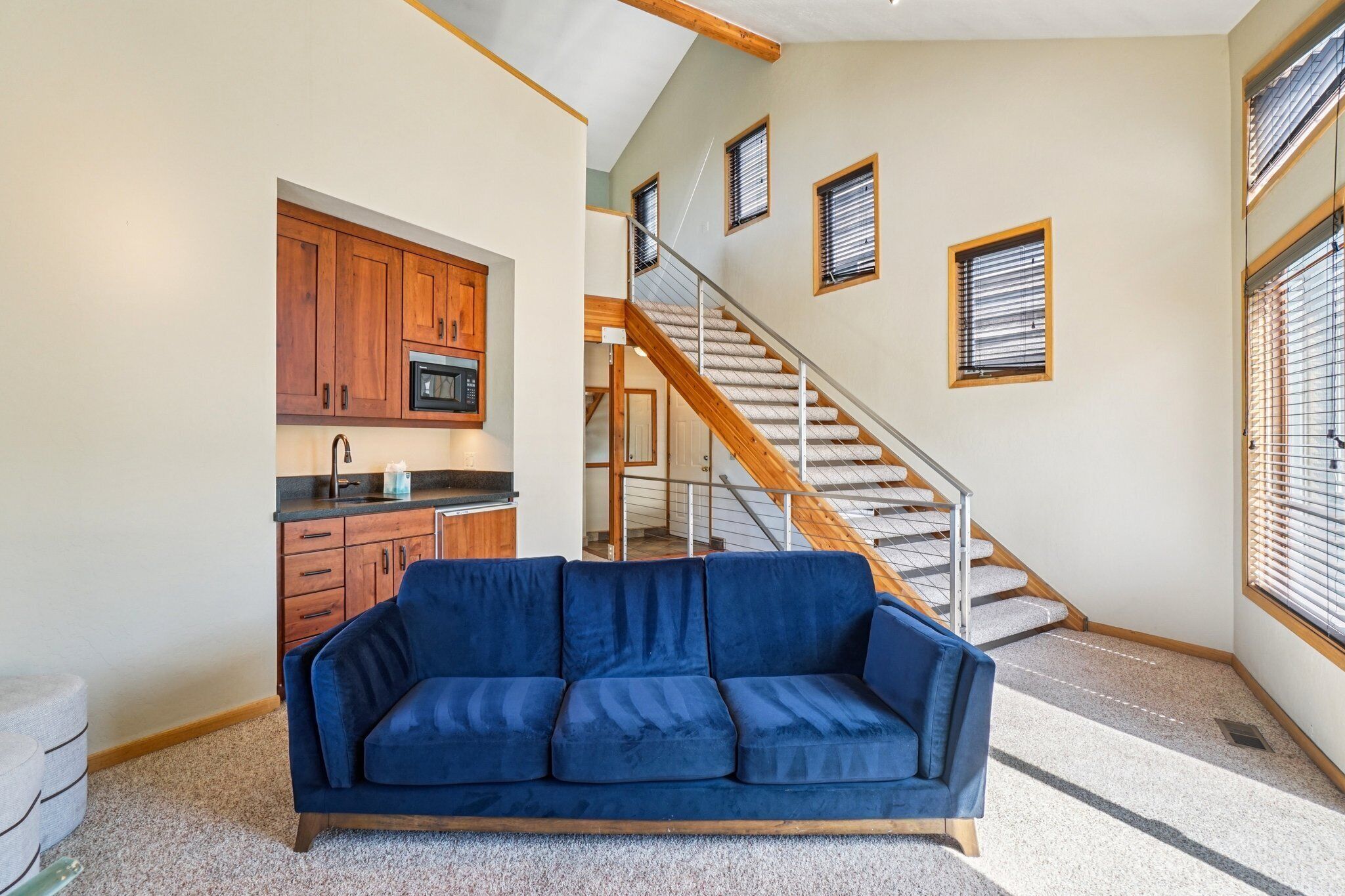 A living room with a blue sofa, a kitchen with wooden cabinets, and a staircase.