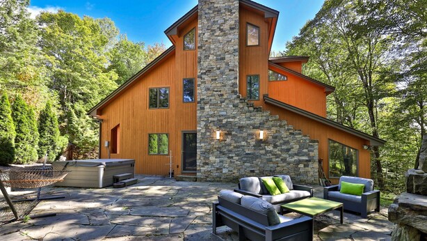 Una casa moderna con fachada de piedra, una terraza amplia y mobiliario exterior.