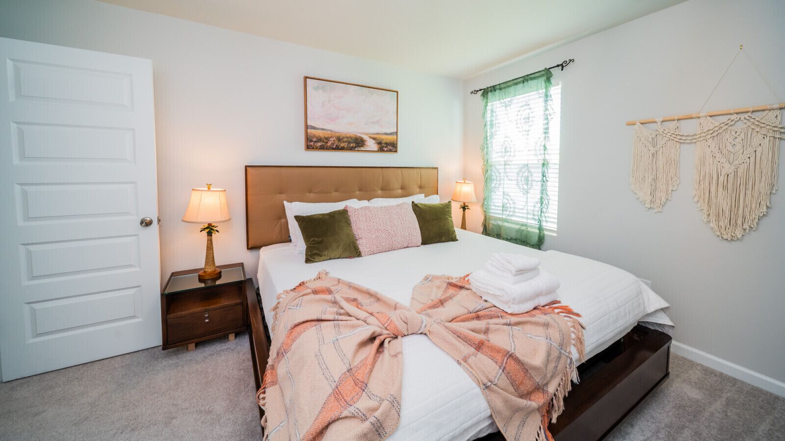 A neatly arranged bedroom with a bed, bedside lamps, a window with curtains, and a door.