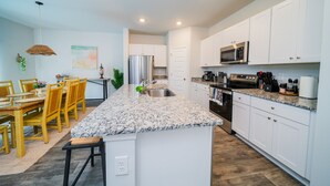 A modern kitchen with white cabinets, granite countertops, stainless steel appliances, and a dining area with yellow chairs and a table.