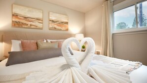 Una habitación de hotel con una cama bien hecha, dos cuadros en la pared y una ventana con cortinas.
