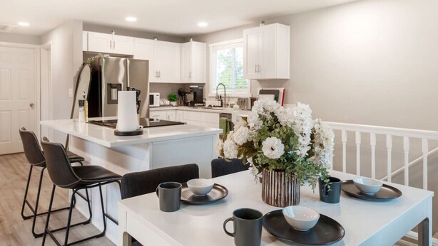 Una cocina moderna con armarios blancos, una isla central y un comedor con mesa y sillas blancas.