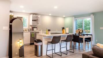 A modern kitchen with a central island, bar stools, and a dining area with a view of the outdoors.